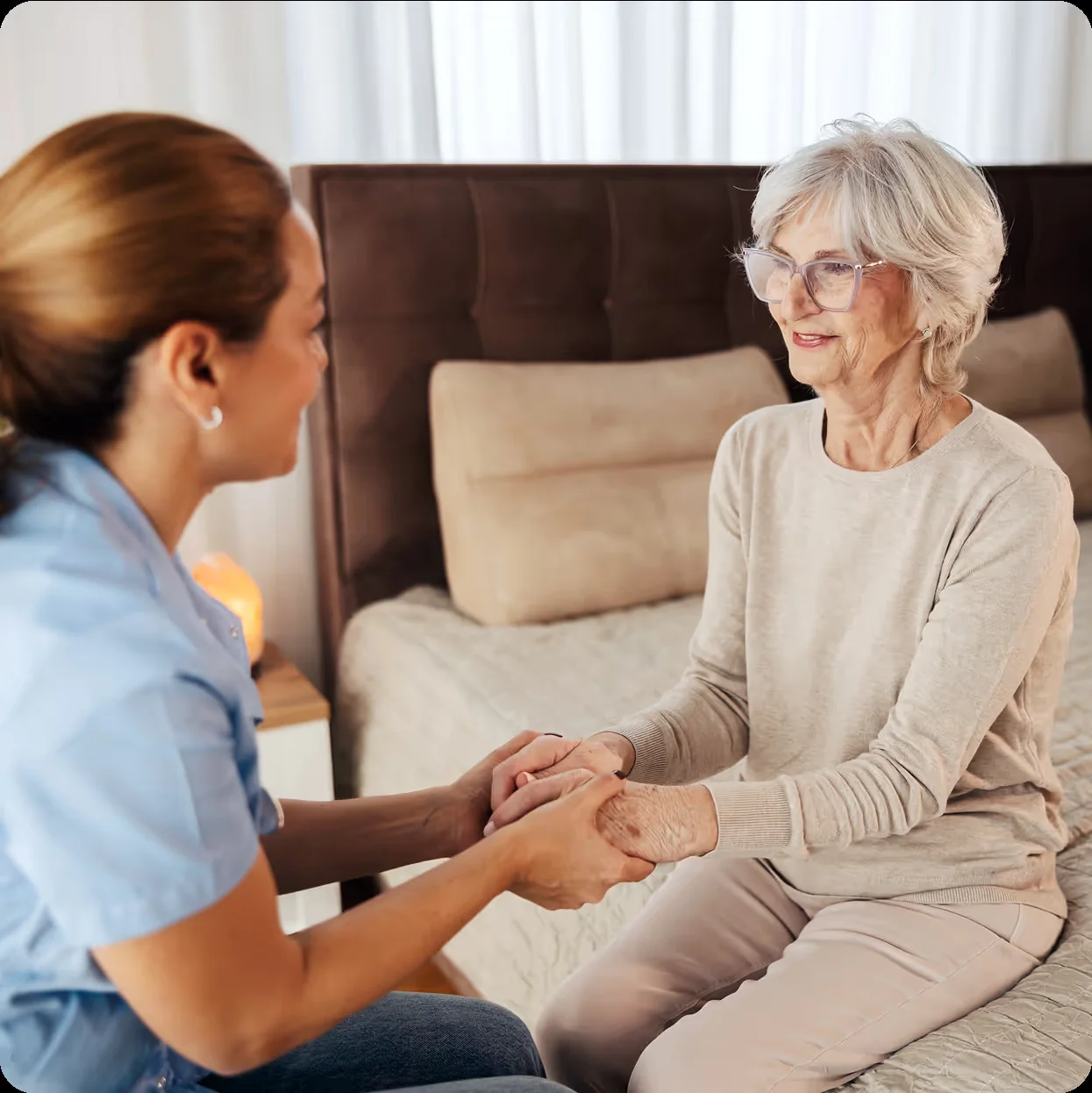 A caregiver holding an older woman’s hands during a conversation